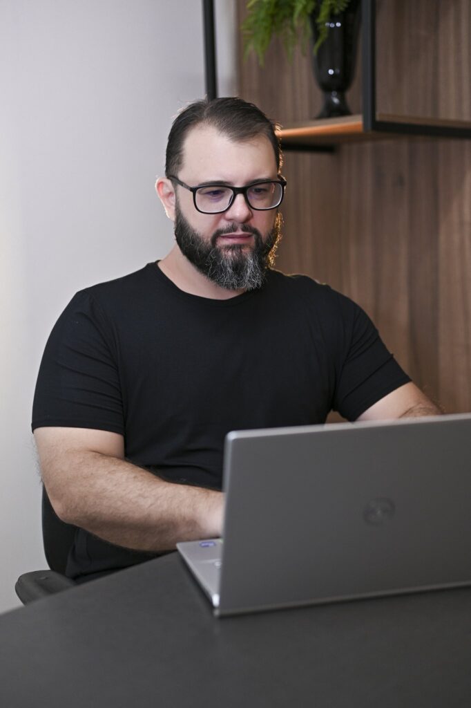 Seated at a dark desk in a black T-shirt, Rodolfo Mendes works at his open laptop.