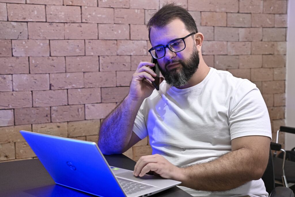 Rodolfo Mendes listens on the phone at his desk, the laptop lid lit blue beside him.